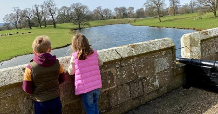 boy and girl with back to camera looking out from Raby Castle's terrace to lake and deer park